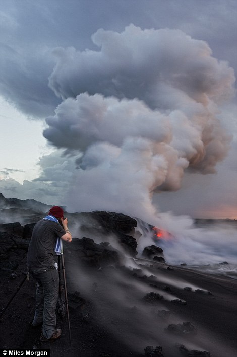 Photographer Ryan Dyar stands on a newly formed beach amongst the still-steaming lava rocks formed by the ocean entry