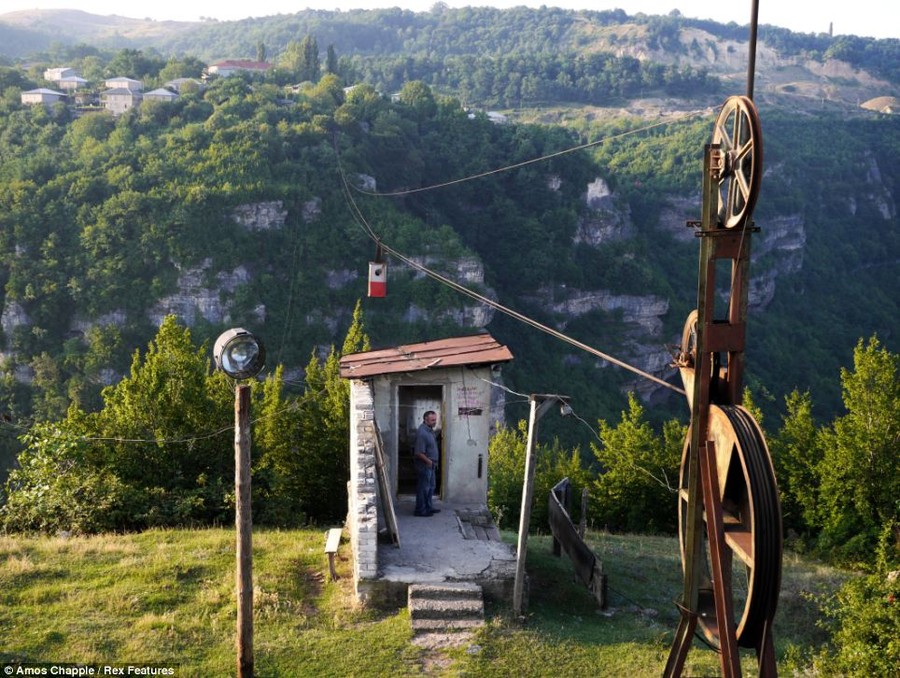 Standing at the platform: A man waits for a cable car to carry him across the gorge. The wheels which operate the system look brown and rusted 